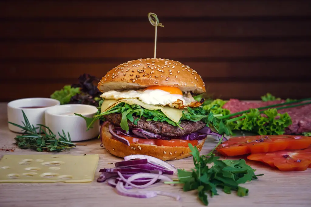 Leckerer Hamburger mit Rindfleisch, Ei, Käse und frischem Gemüse auf einem Holzbrett